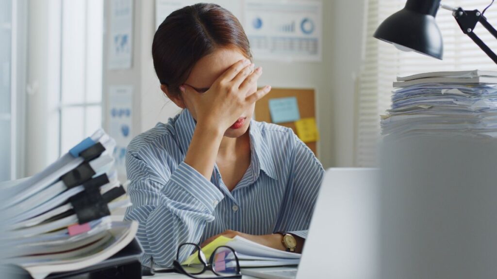 Woman sitting at her desk filled with work looking stressed