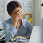Woman sitting at her desk filled with work looking stressed
