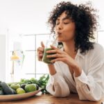 Young woman drinking green juice at a table with healthy food