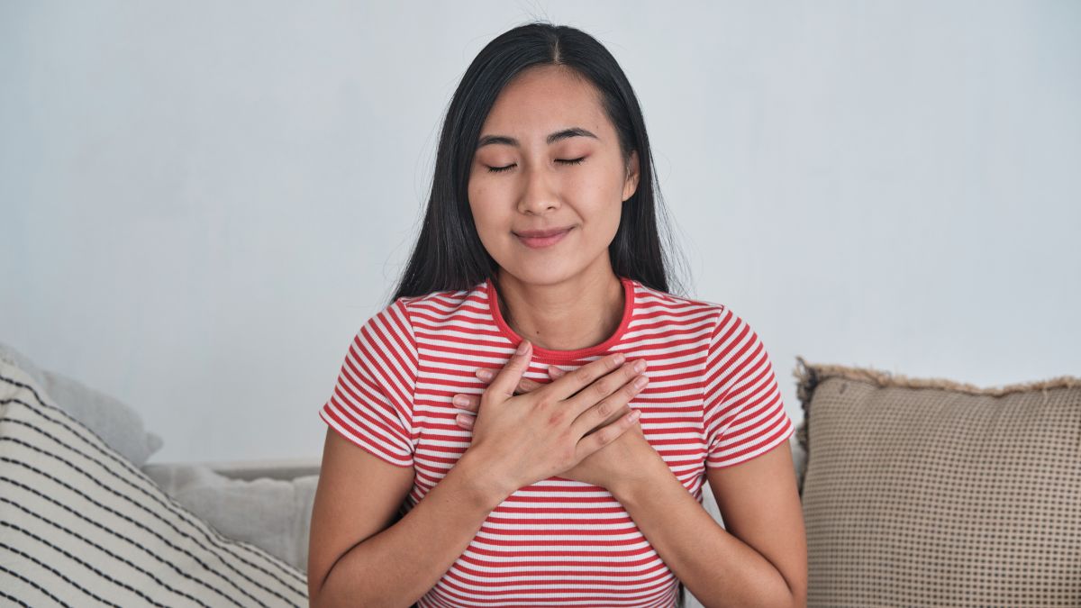 Young woman sitting on the couch with her hands to her chest and eyes closed