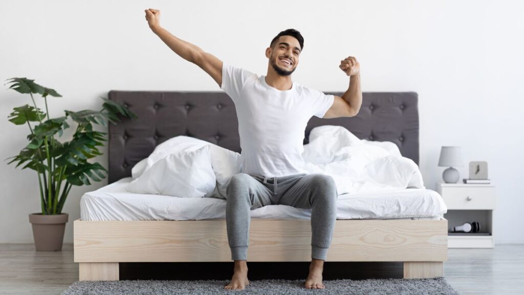Man stretching while sitting on his bed as he wakes up