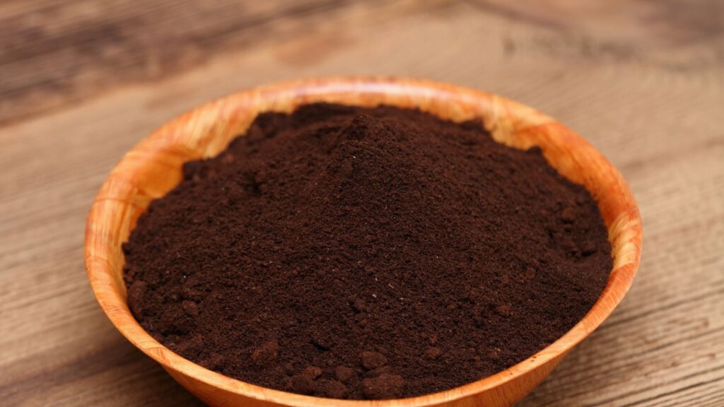 Wooden bowl filled with coffee grounds on table