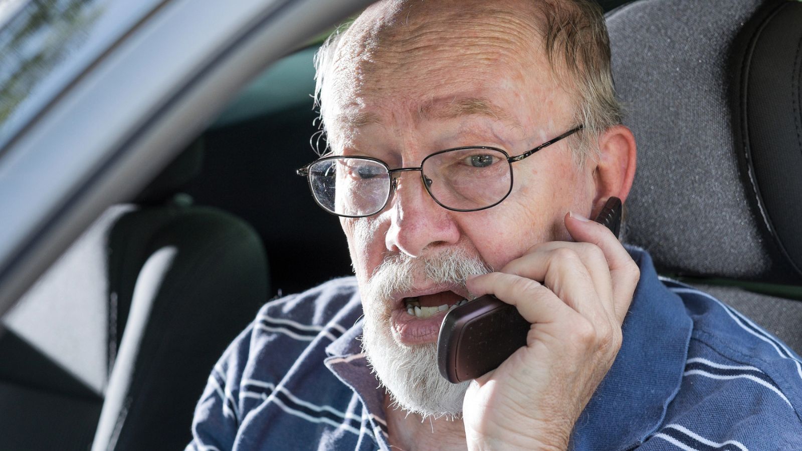 Old man sitting in a car using a cell phone
