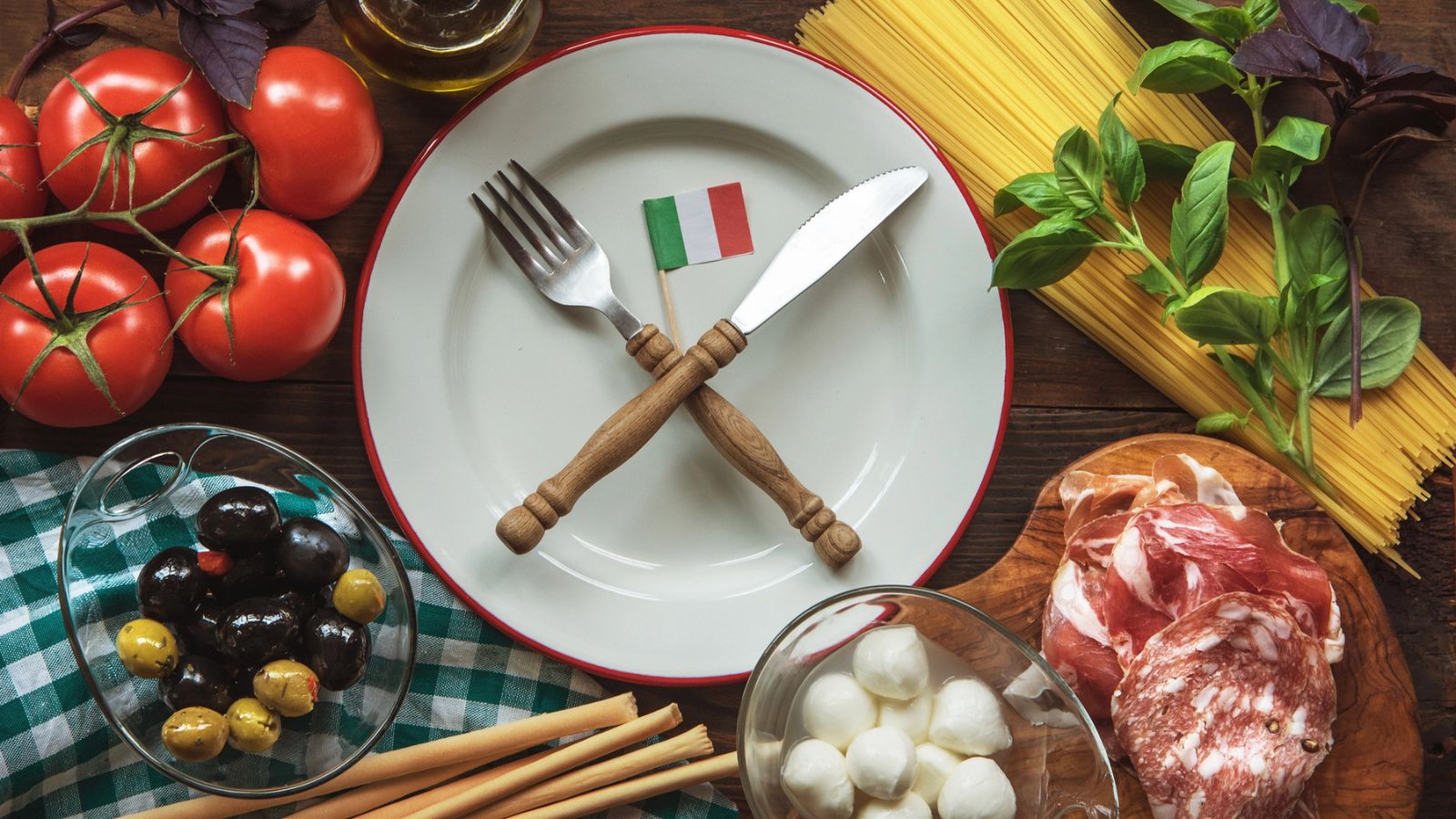 Table filled with Italian food, a plate with utensils and an Italian flag