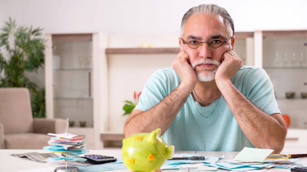 Older man sitting at the table with a piggy bank looking annoyed
