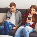 Couple sitting on the couch using their cell phones