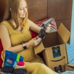 Woman sitting on her bed opening a box of snacks from Amazon