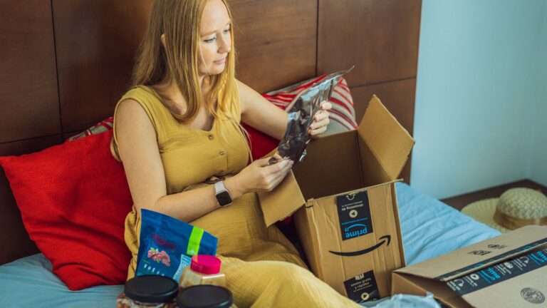 Woman sitting on her bed opening a box of snacks from Amazon