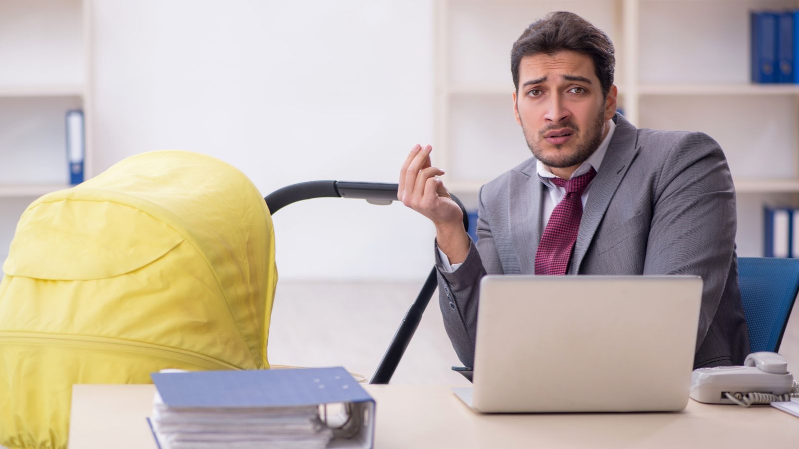 Exhausted dad sitting at desk with stroller next to him