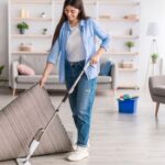 Woman mopping her floor while holding up the rug