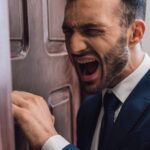 Man in a suit leaning against a door looking like he's yelling