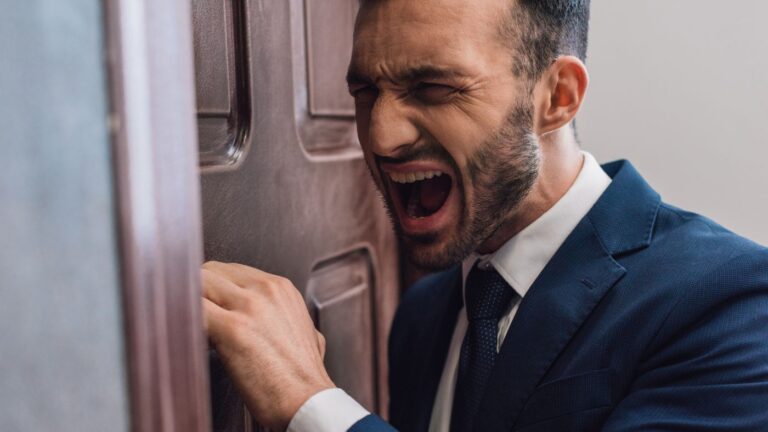 Man in a suit leaning against a door looking like he's yelling