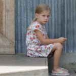Young girl sitting alone on a step looking annoyed