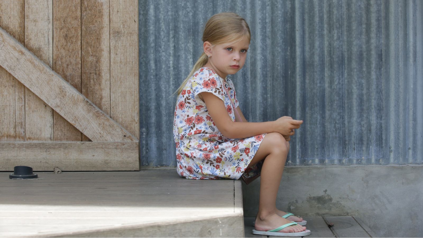 Young girl sitting alone on a step looking annoyed