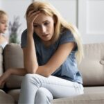 Nanny sitting on the couch looking stressed with a child behind her