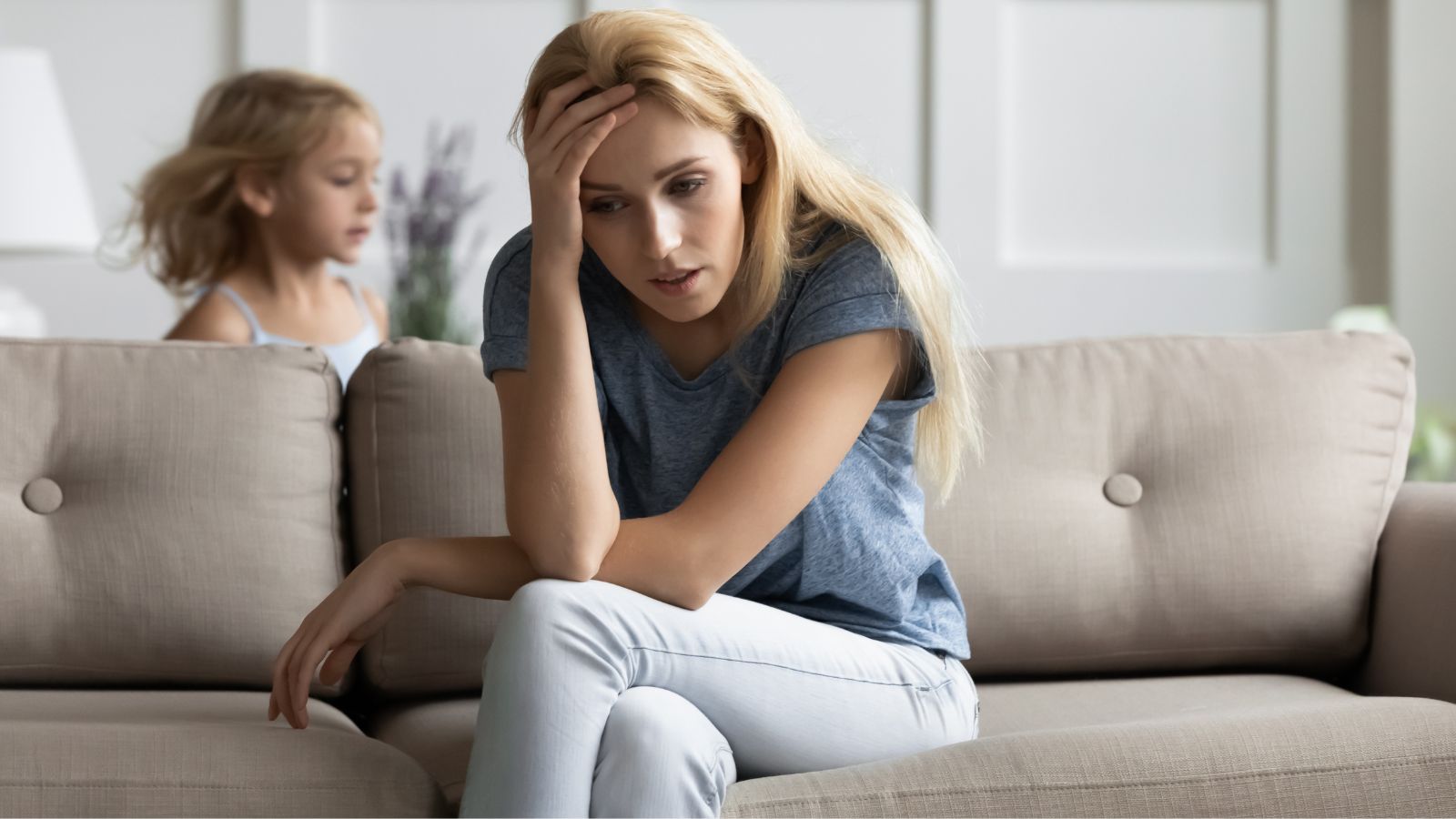 Nanny sitting on the couch looking stressed with a child behind her