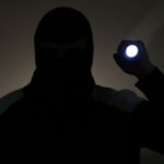 Man in the dark dressed in dark clothes holding a flashlight