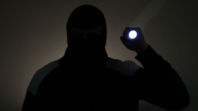 Man in the dark dressed in dark clothes holding a flashlight