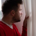 Man peering through curtains out the window