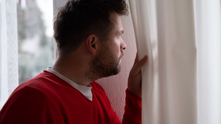 Man peering through curtains out the window