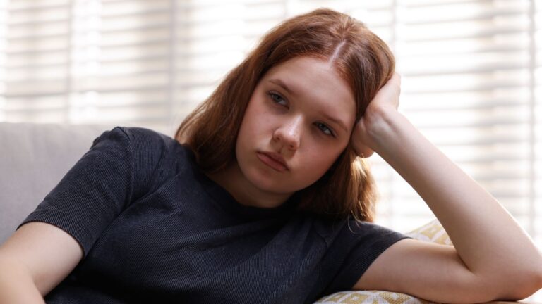 Teenage girl sitting on couch looking sad