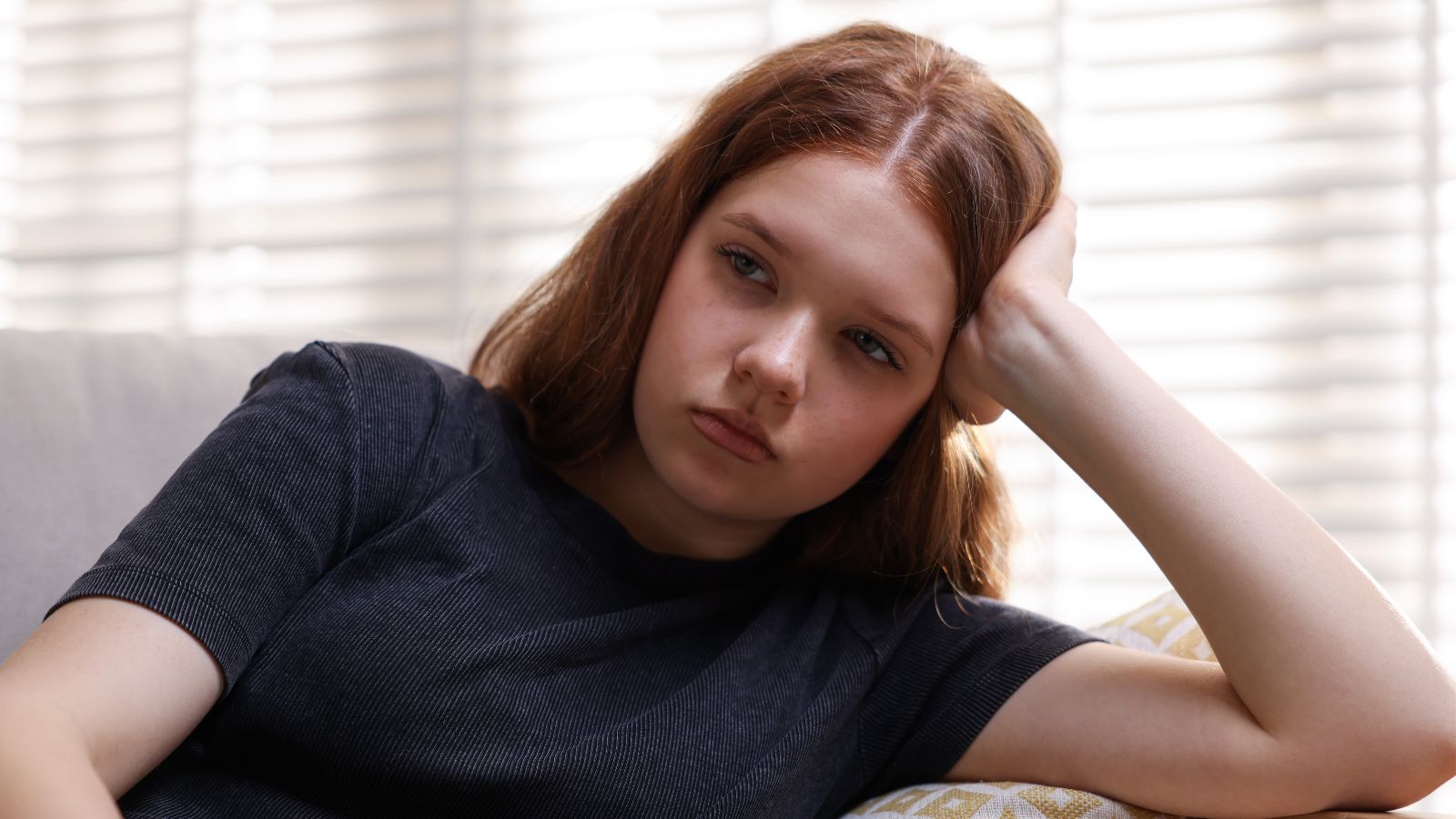 Teenage girl sitting on couch looking sad