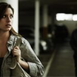 Woman looking scared as a man dressed in black is walking behind her