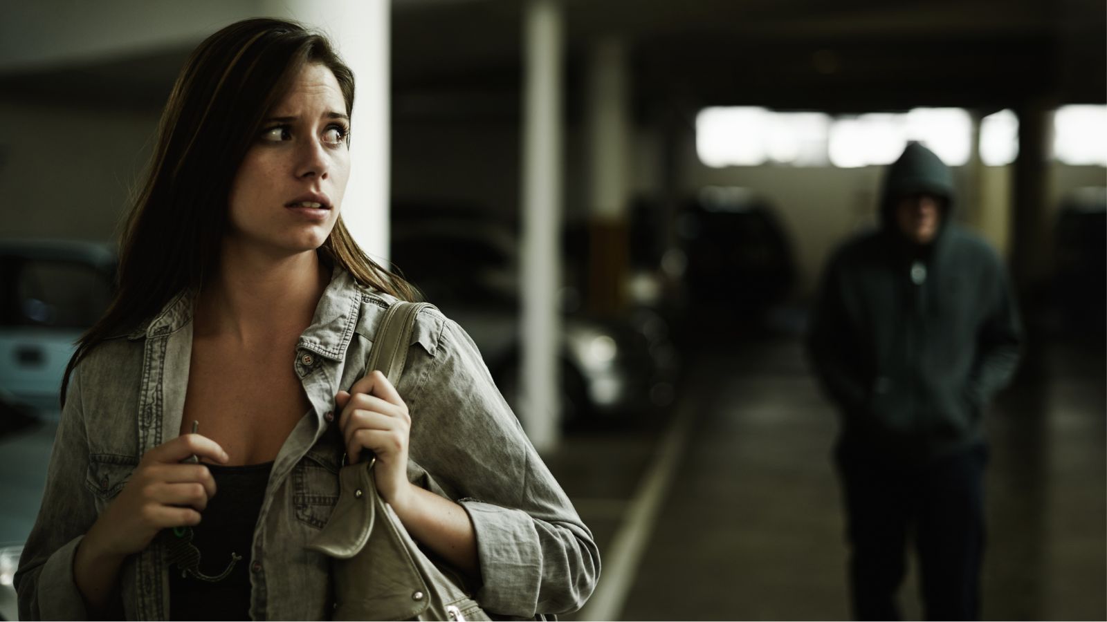 Woman looking scared as a man dressed in black is walking behind her