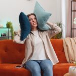 Woman covering her ears with pillows and looking angry
