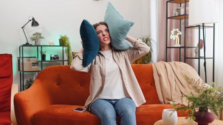 Woman covering her ears with pillows and looking angry