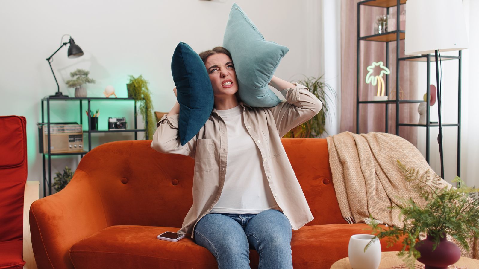 Woman covering her ears with pillows and looking angry