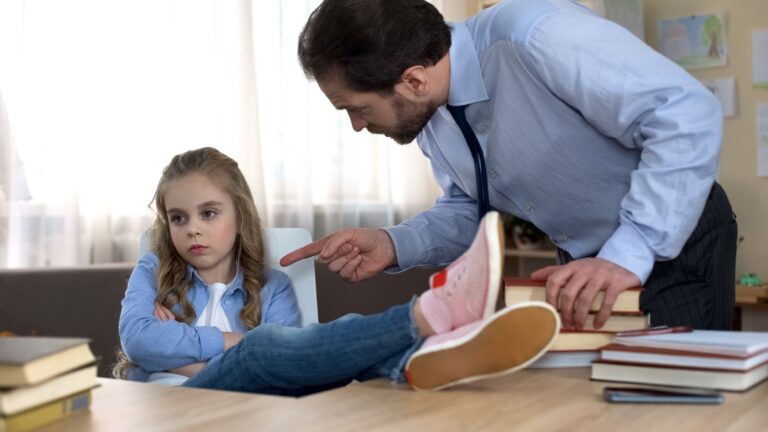 Father yelling at preteen girl sitting at desk