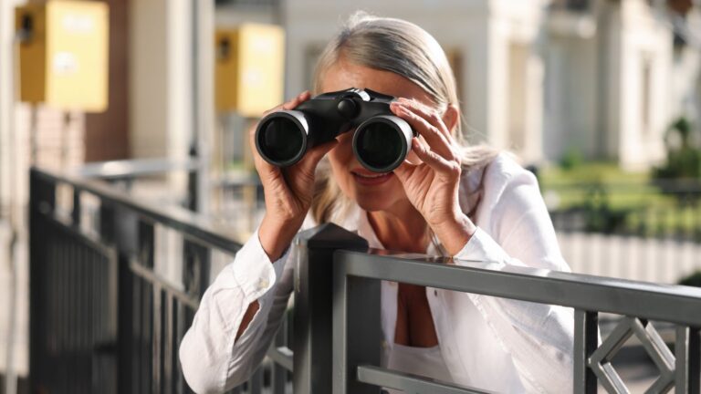 Older woman watching her neighbor with binoculars