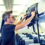 Man putting his bag into the overhead compartment on plane