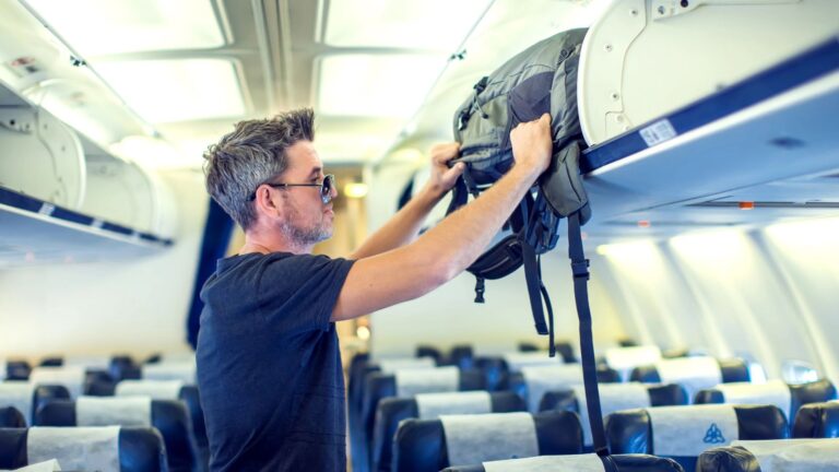 Man putting his bag into the overhead compartment on plane