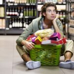 Guy sitting on the floor of the supermarket with a basket full of food