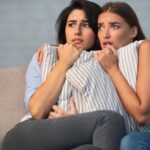 Two women sitting scared on the couch together