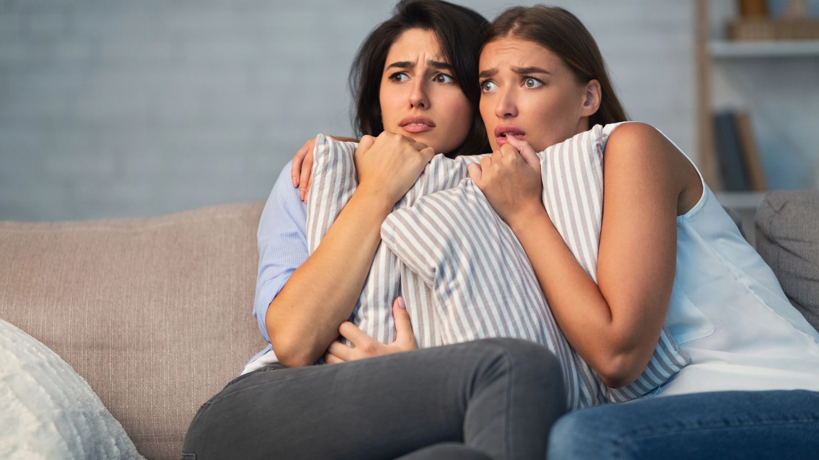 Two women sitting scared on the couch together