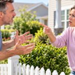 Male and female neighbor arguing with each other over a white picket fence